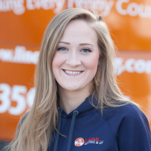 Christie S., Sales Coordinator at Lincoln Heating & Air, smiling in company hoodie with orange service vehicle background.