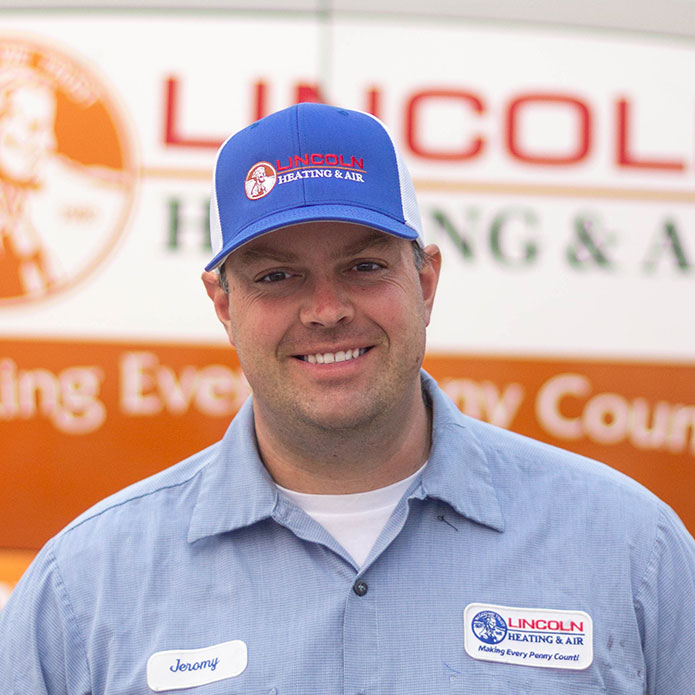 Jeromy C., service technician at Lincoln Heating & Air, smiling in uniform with company logo in background, representing family-oriented heating and cooling services.