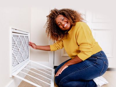 Woman smiling while replacing an air filter in a home, demonstrating a key maintenance tip for improving indoor air quality and reducing allergy symptoms.