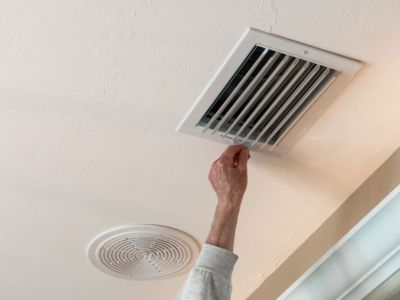 Hand adjusting a ceiling air vent in a home, illustrating central air conditioning system maintenance and functionality.