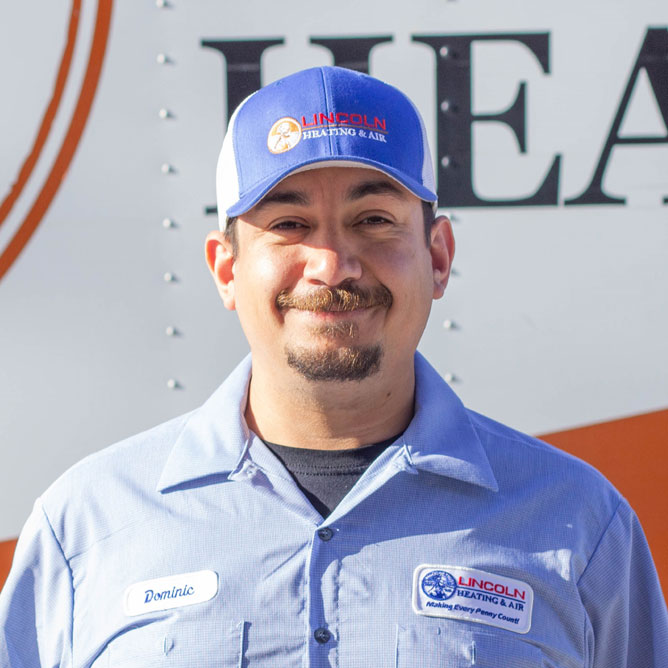 Service technician Dominic E. wearing a Lincoln Heating & Air uniform and cap, smiling in front of a company vehicle, representing the family-oriented team dedicated to heating and cooling services.