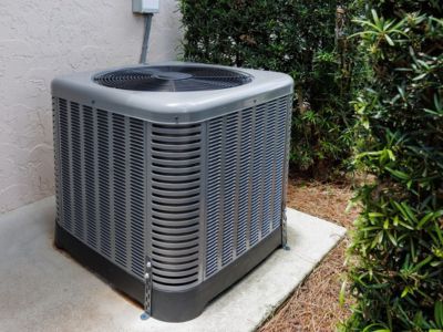 Air conditioning unit outside a home, surrounded by greenery, illustrating the importance of routine AC maintenance for extending lifespan and preventing repairs.