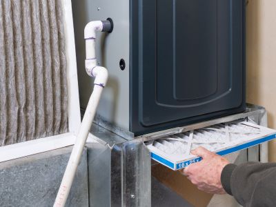 Hand inserting a new air filter into a heating system, highlighting maintenance tasks essential for efficient operation and longevity of heating units.