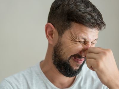 Man grimacing while pinching his nose, indicating discomfort from unusual smells, relevant to signs of heating system issues for homeowners.
