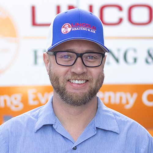 A man in a collared shirt wears a blue and white cap with "LINCOLN HEATING & AIR," showcasing the heating and air team.