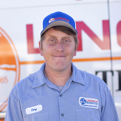 Cory, a technician at Lincoln Heating & Air, smiles in a blue cap and work shirt in front of the company logo.